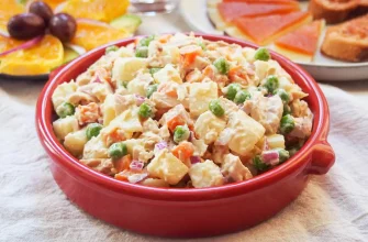 Ensaladilla rusa tradicional española con patatas, zanahorias, guisantes, atún y mayonesa servida en un plato blanco.