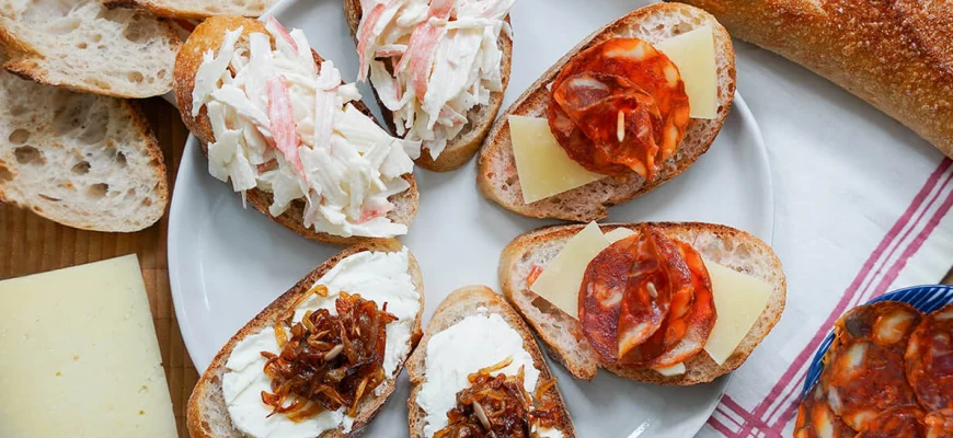 Pintxos españoles de queso de cabra, caranguejo y chorizo en baguettes, servidos como aperitivos.