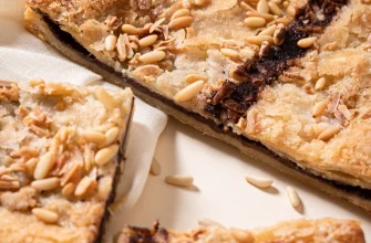 Coca de hojaldre catalana con chocolate, decorada con piñones y almendras.