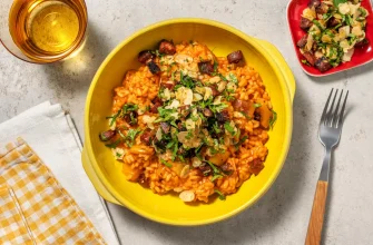 Paella española inspirada, con chorizo, pimiento rojo, almendras y toque de limón, en un plato blanco sobre mesa de madera.